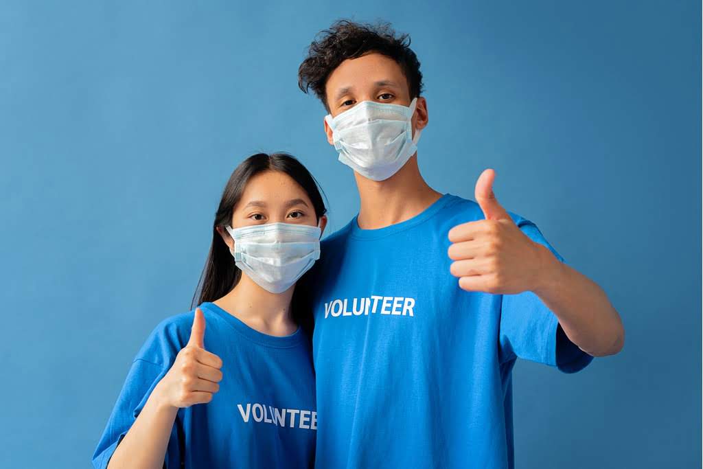 2 volunteers in blue shirts and masks giving a thumbs-up