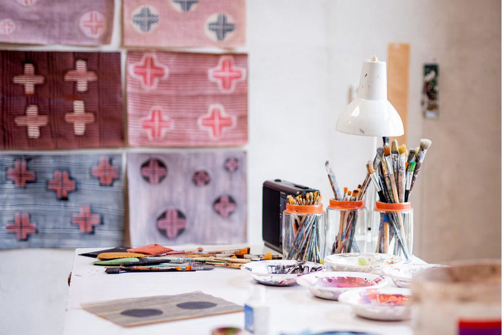 Paintbrushes in glasses and paint on a white countertop