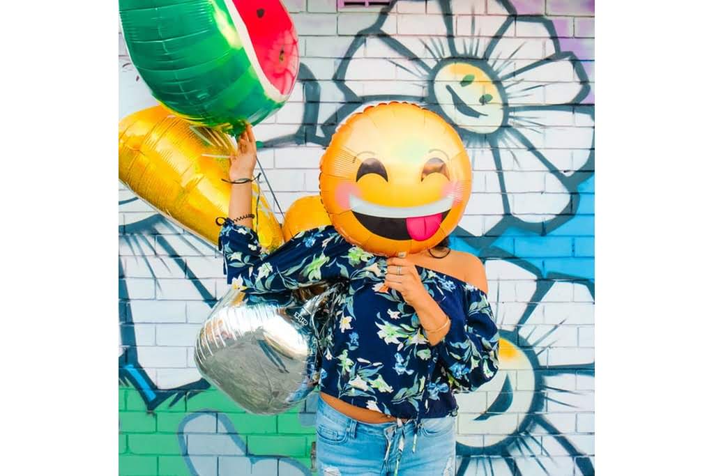 A woman in a blue shirt holding various balloons in front of a floral wall