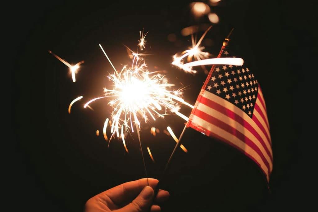 A sparkler and an American flag held up by a hand