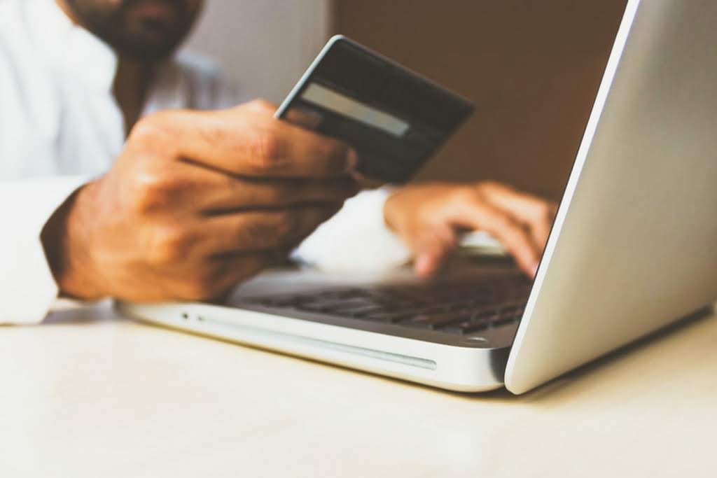 A man holding a credit card up next to a laptop