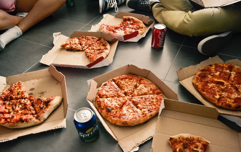 Pizzas in boxes all over the ground next to soda cans