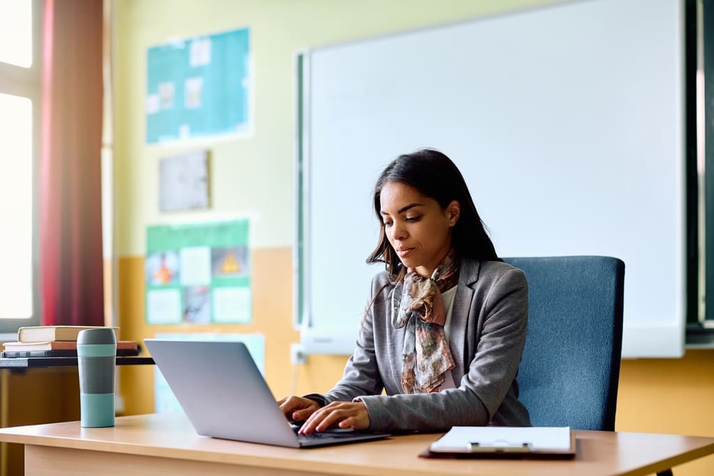 Teacher using template on laptop to create thank-you letter for fundraising volunteers in classroom