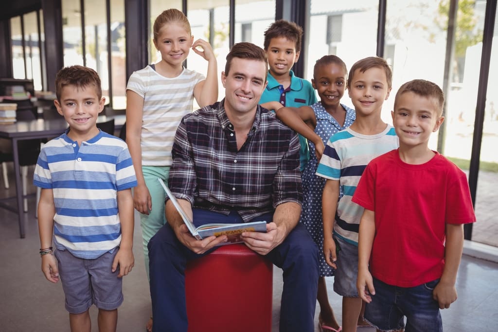 Teacher holding classroom memory book surrounded by students