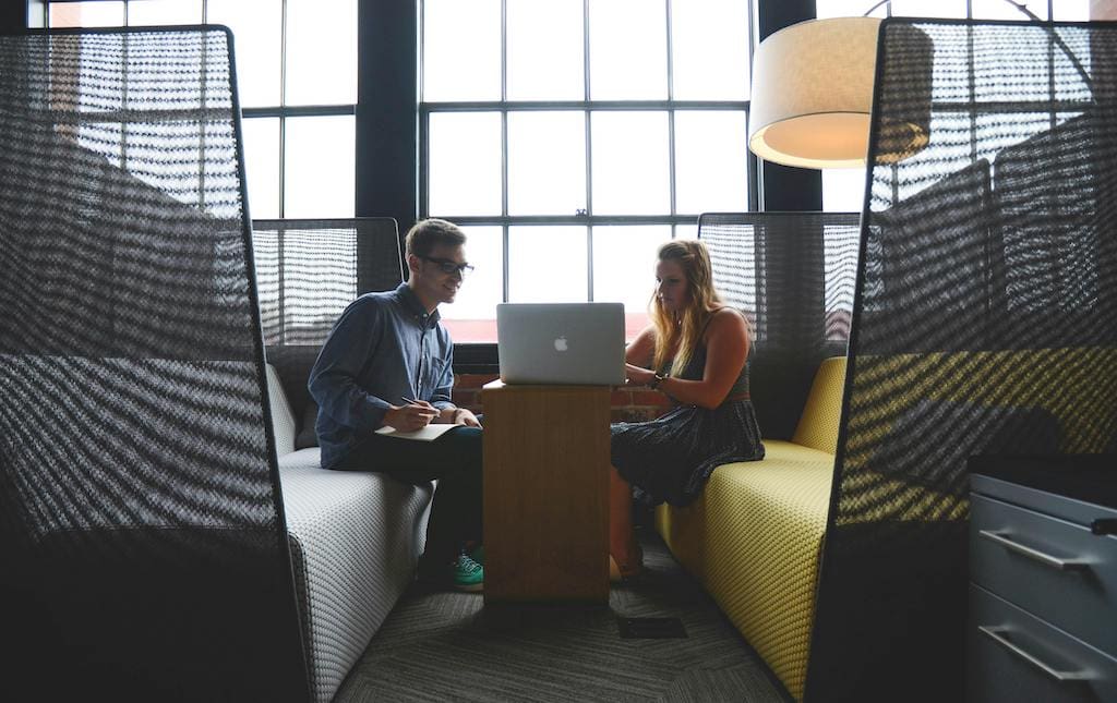 Two young people talking and working on a laptop