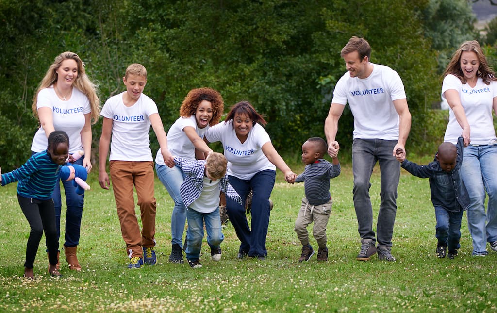 Volunteers playing with young children outside on green grass