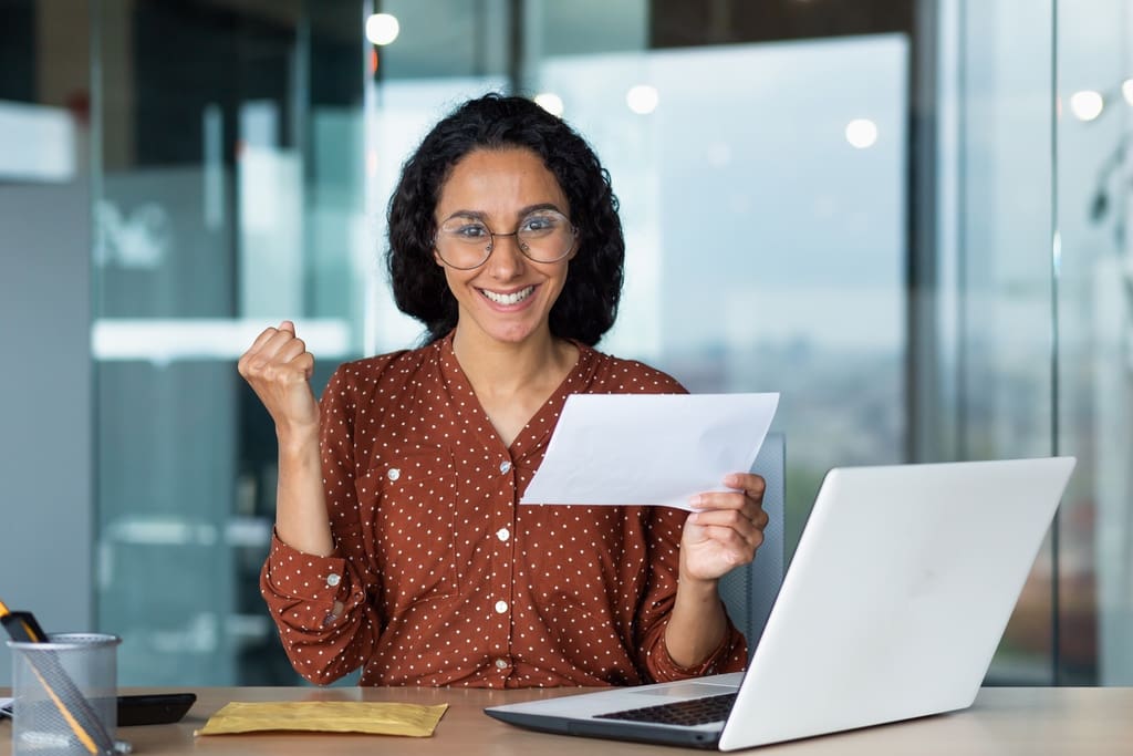 Teacher holding sheet of paper in front of laptop to symbolize preparing letter to send to donors