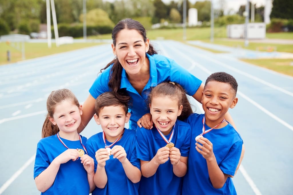 K-12 students posing with participation medals and member of fun run company at athletic field