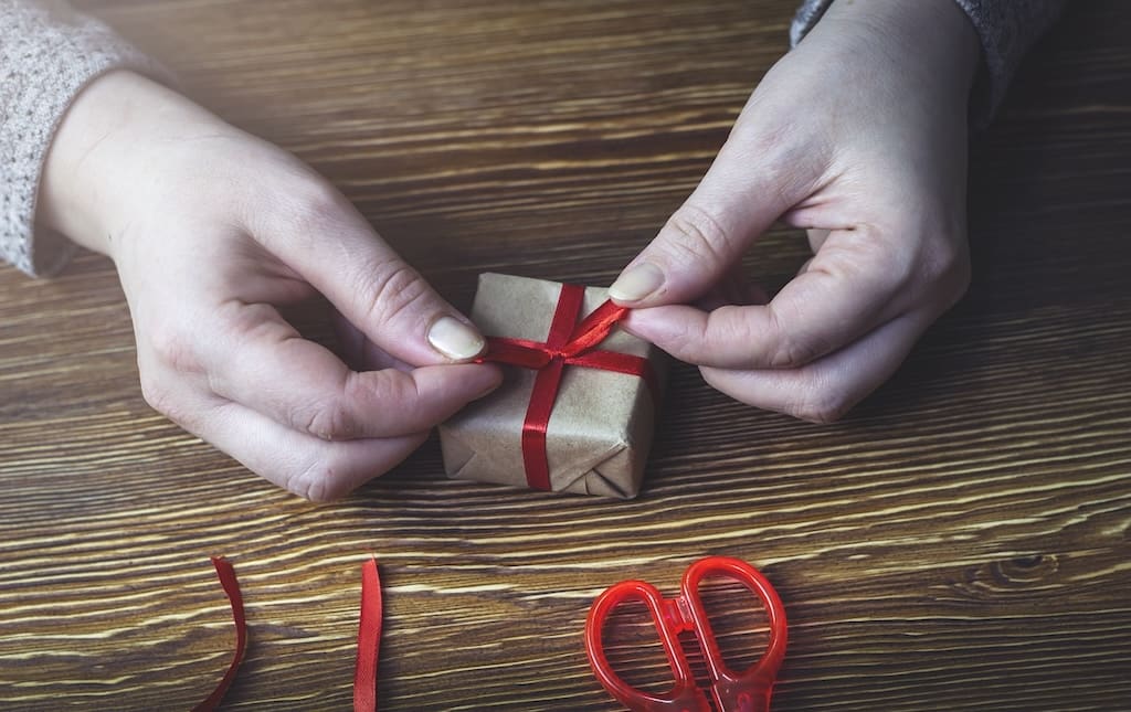 Two hands wrapping a small Christmas gift