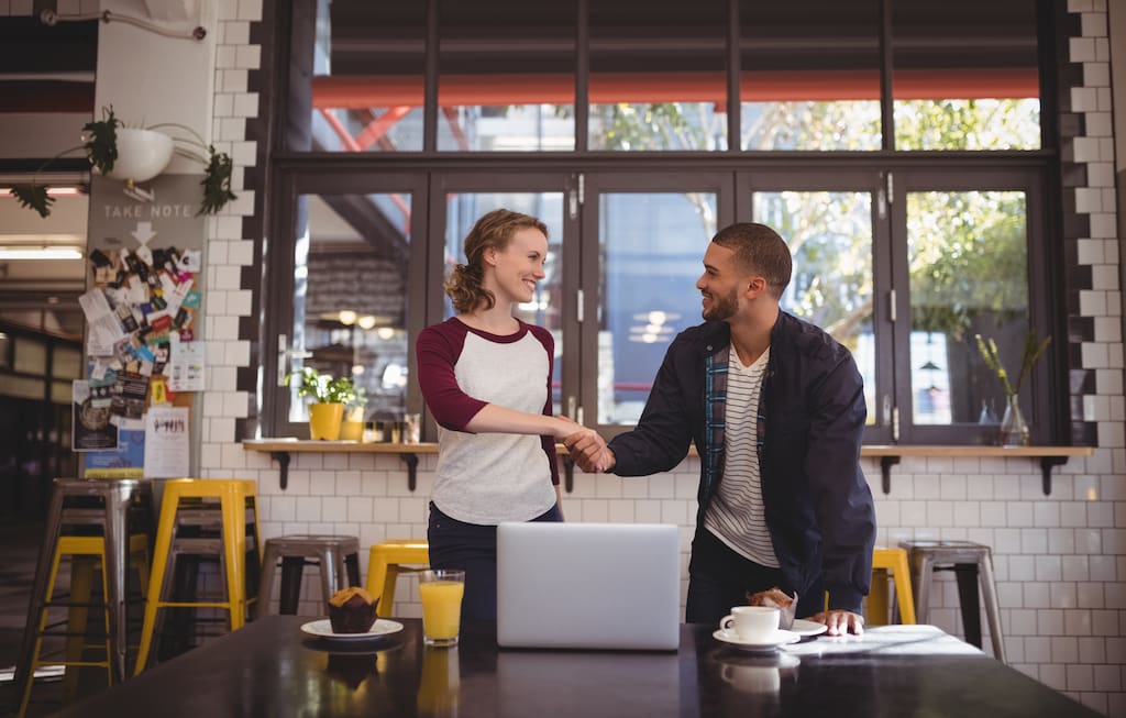 PTA organizer shaking hands with a potential sponsor in a cafe